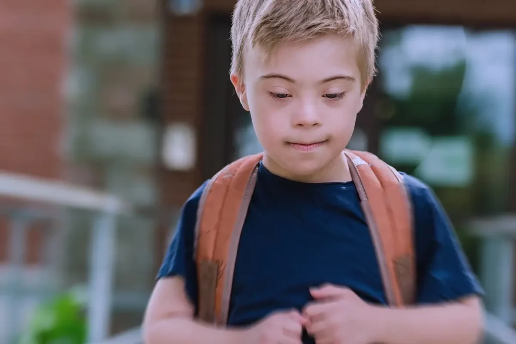 Bambino con disabilità intellettiva che indossa uno zaino, assorto nei suoi pensieri mentre cammina in un contesto scolastico